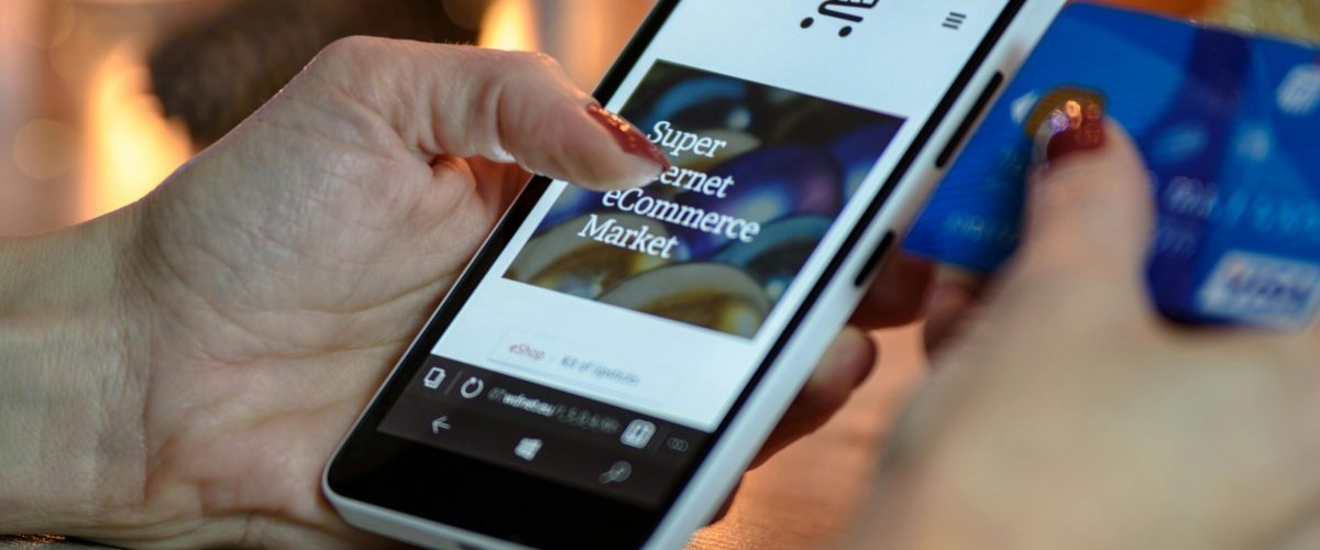 Woman using smartphone for online shopping with credit card in hand, festive background lighting.